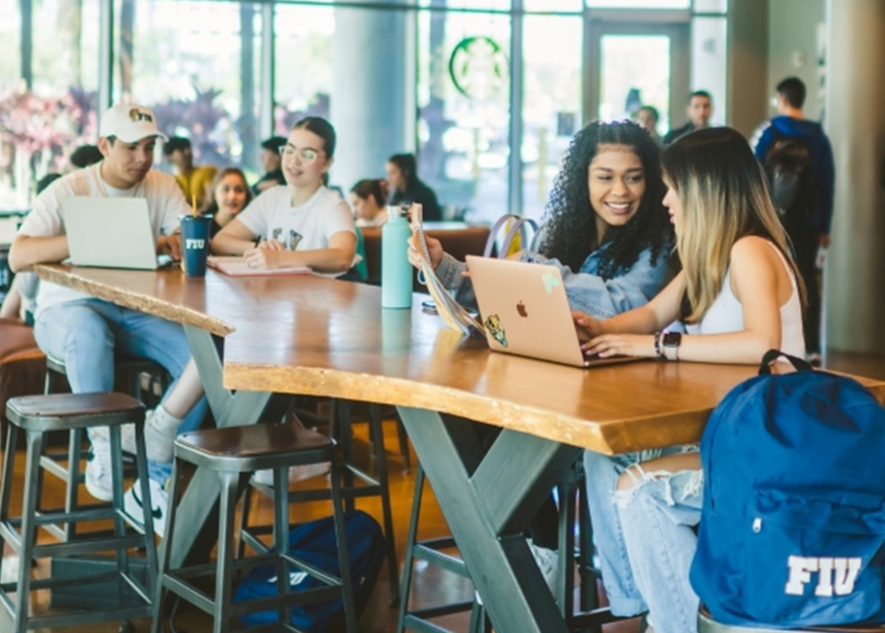 Four students sit at table in MANGO building Starbucks with computers