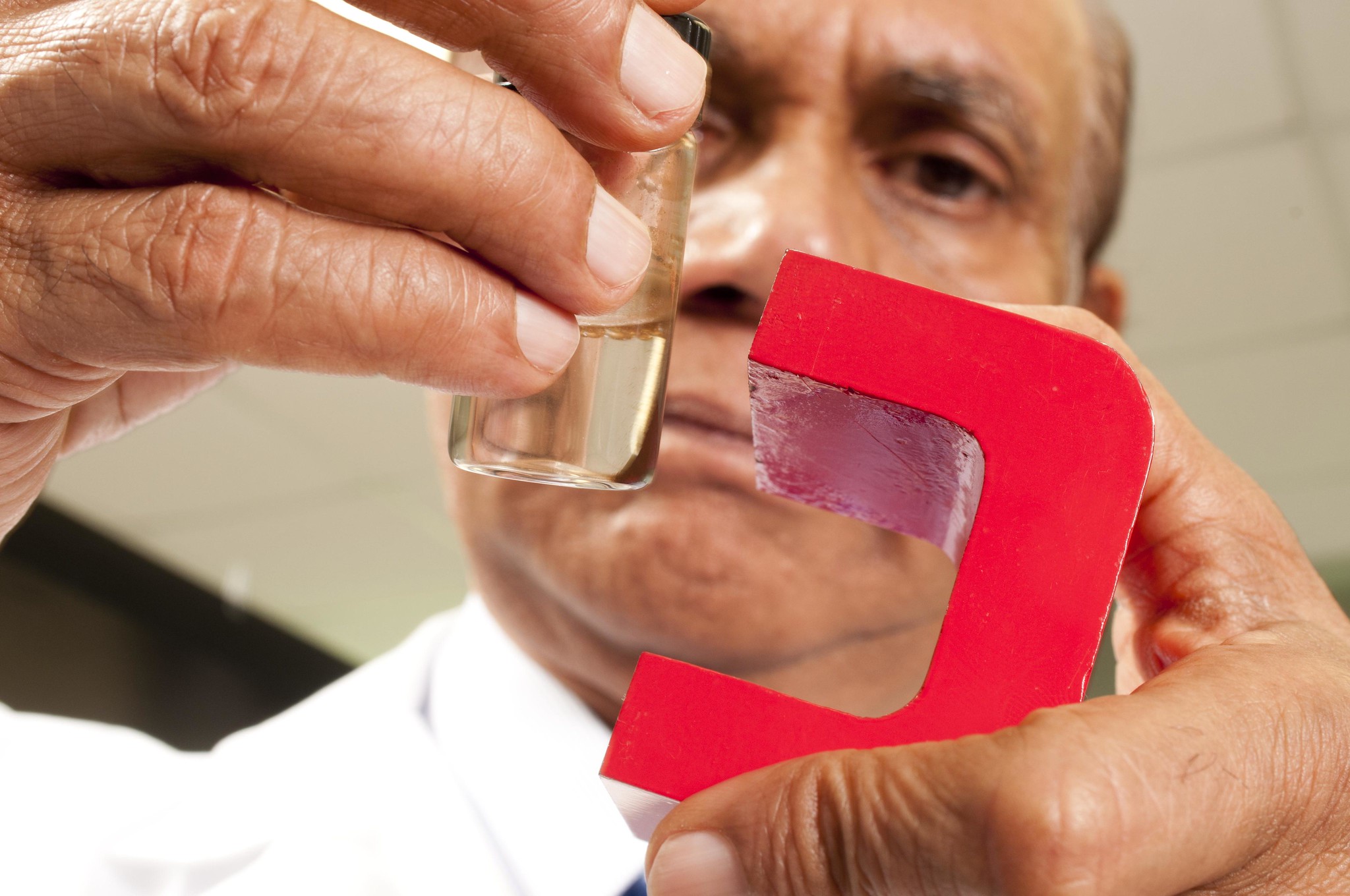 Researcher Madhavan Nair holding glass flask and magnet.