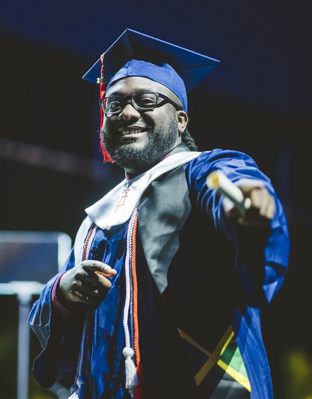 Graduate with Jamaica stole smiling and pointing at camera