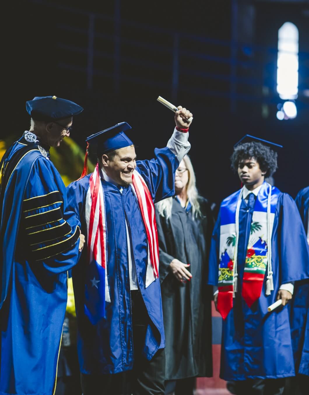 Graduate with Puerto Rico stole grinning and holding diploma up