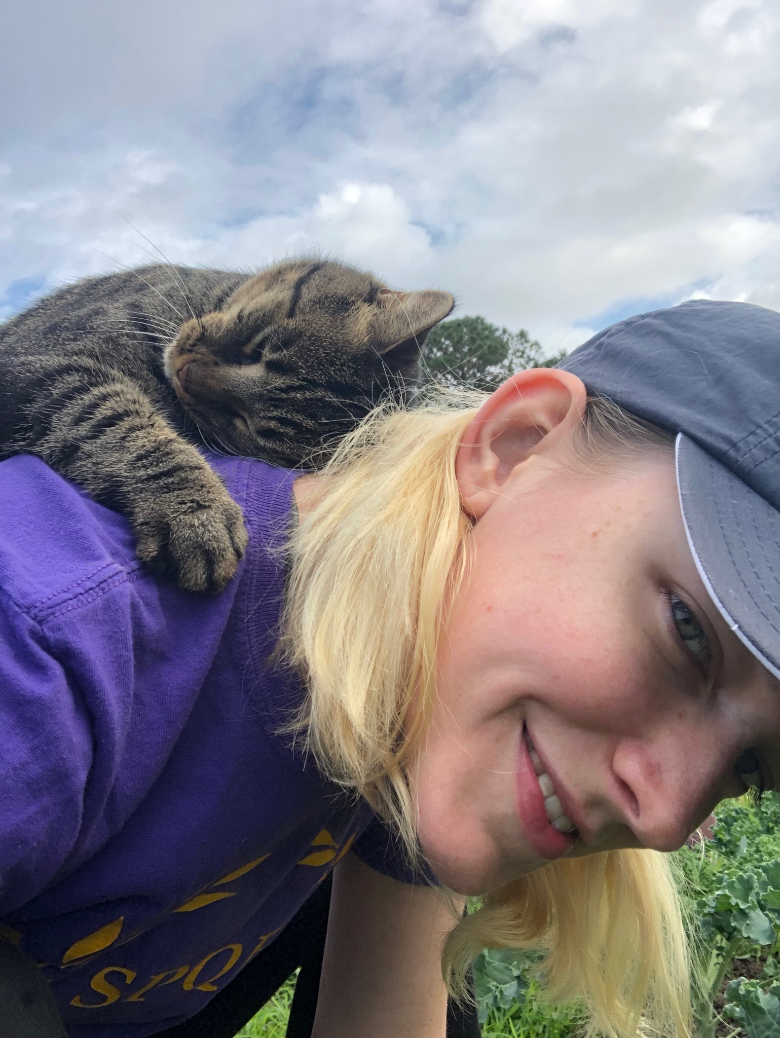 Corgan harvests vegetables while a cat relaxes on her back