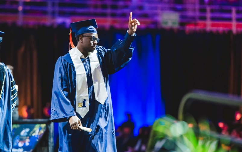 Graduate with diploma holding up index finger, giving thanks to God