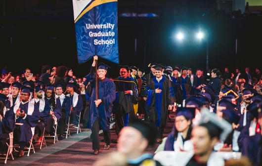 Faculty and staff walking into commencement with banner