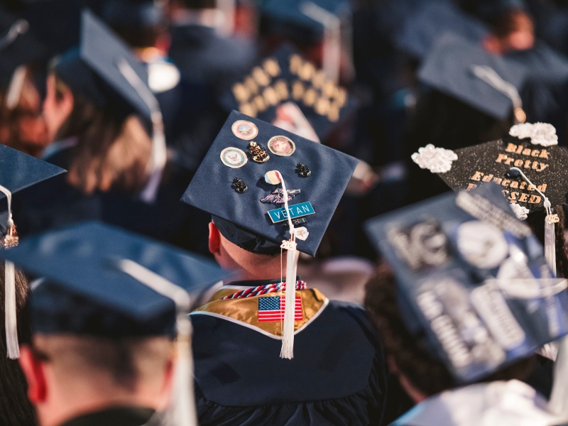 Photo of graduate sitting with his cap decorated with Veterans emblems. 