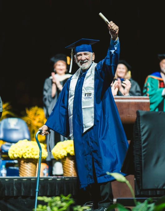 85-year-old graduate holding up his diploma on stage 