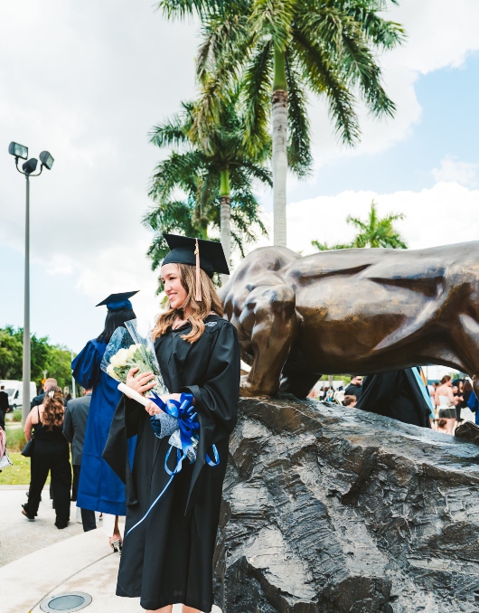 Graduate celebrating next to Panther statue and holding flowers she was given